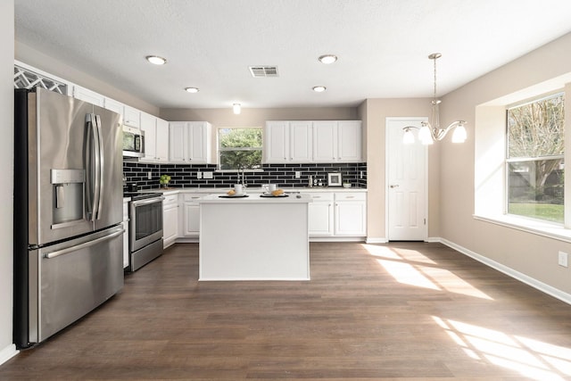 kitchen with appliances with stainless steel finishes, a center island, white cabinetry, hanging light fixtures, and a chandelier