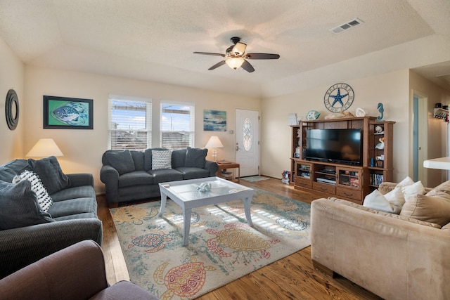 living room featuring a raised ceiling, wood-type flooring, a textured ceiling, and ceiling fan