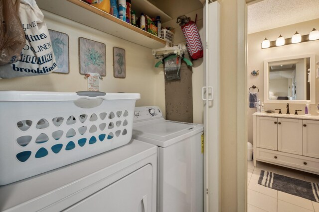 washroom with a textured ceiling, light tile patterned floors, washer and dryer, and sink