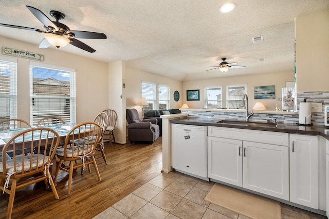 kitchen with dark countertops, open floor plan, white dishwasher, white cabinetry, and a sink