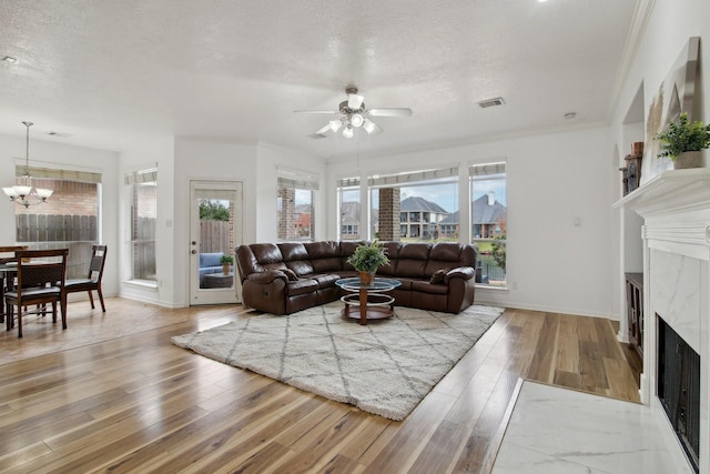 living room with wood-type flooring, a fireplace, ceiling fan with notable chandelier, and a textured ceiling