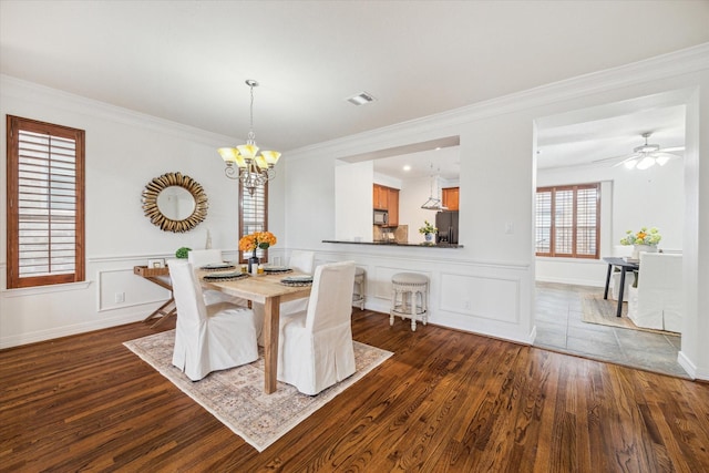 dining space with dark wood-type flooring, ceiling fan with notable chandelier, and ornamental molding