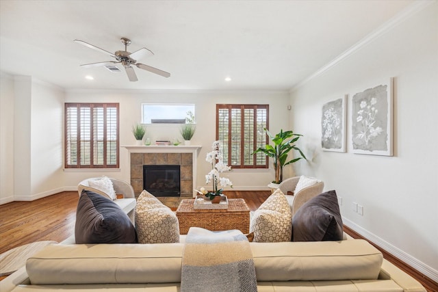 living room with a healthy amount of sunlight, a tiled fireplace, crown molding, and hardwood / wood-style floors