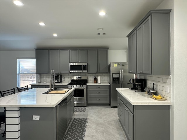 kitchen with appliances with stainless steel finishes, gray cabinetry, and a center island with sink