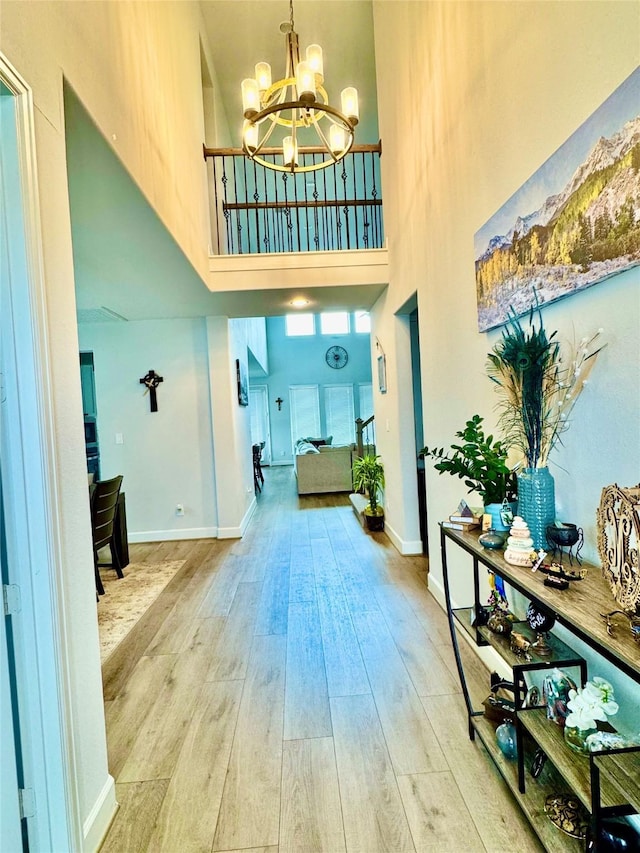 foyer entrance featuring light hardwood / wood-style floors, a towering ceiling, and an inviting chandelier