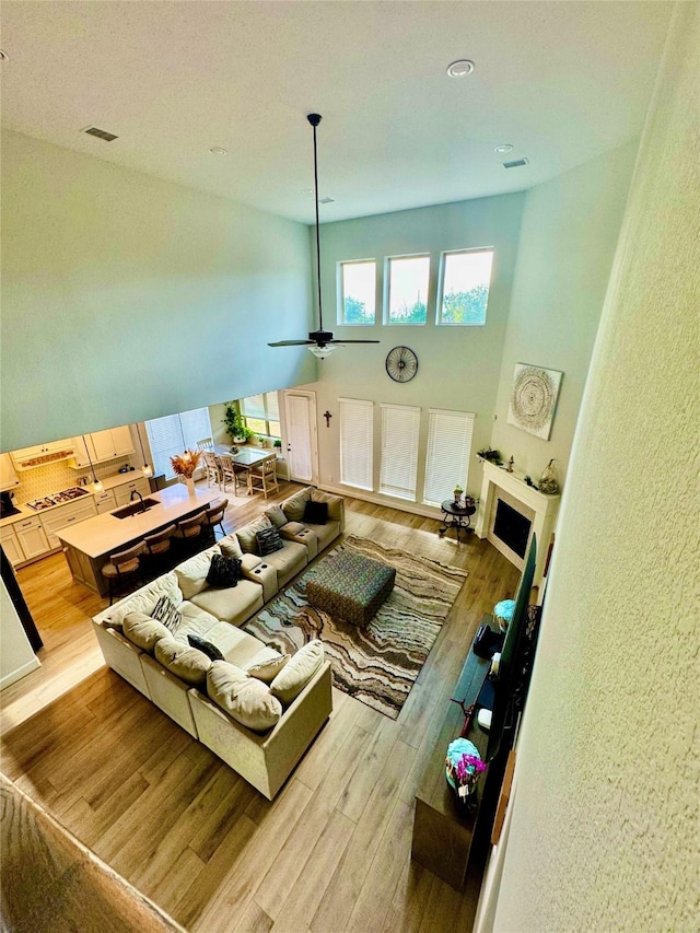 living room featuring ceiling fan, light wood-type flooring, a towering ceiling, and sink