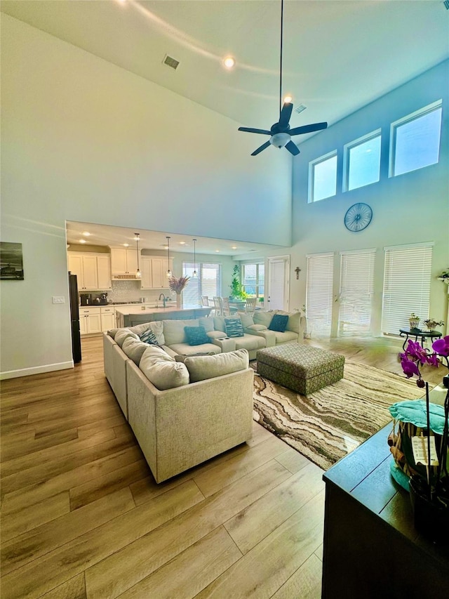 living room featuring ceiling fan, light hardwood / wood-style floors, a towering ceiling, and sink