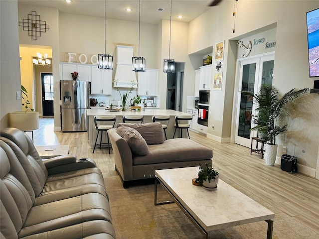 living room with baseboards, a towering ceiling, an inviting chandelier, french doors, and light wood-style floors