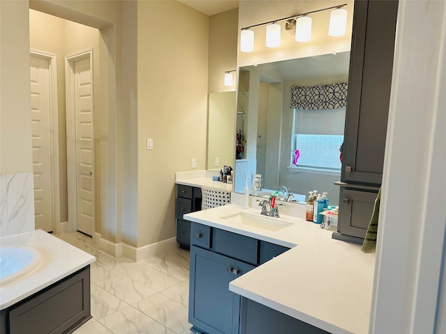 bathroom with marble finish floor, baseboards, two vanities, and a sink