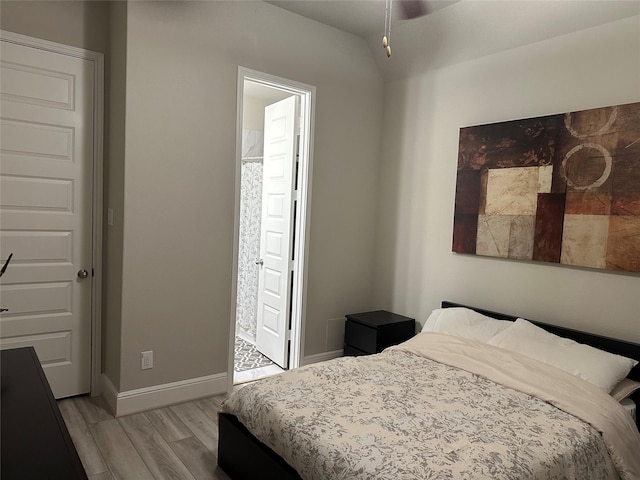 bedroom featuring light wood-style floors, lofted ceiling, connected bathroom, and baseboards