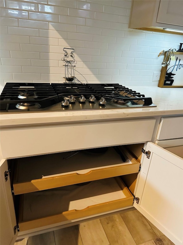 interior details with light countertops, stainless steel gas stovetop, light wood-style flooring, and decorative backsplash