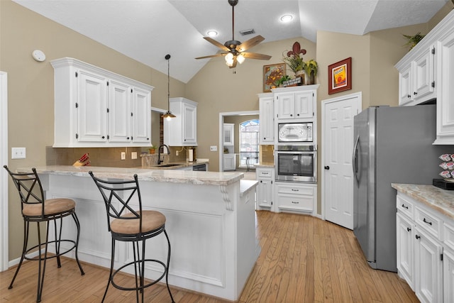 kitchen with white cabinetry, appliances with stainless steel finishes, a kitchen breakfast bar, and kitchen peninsula