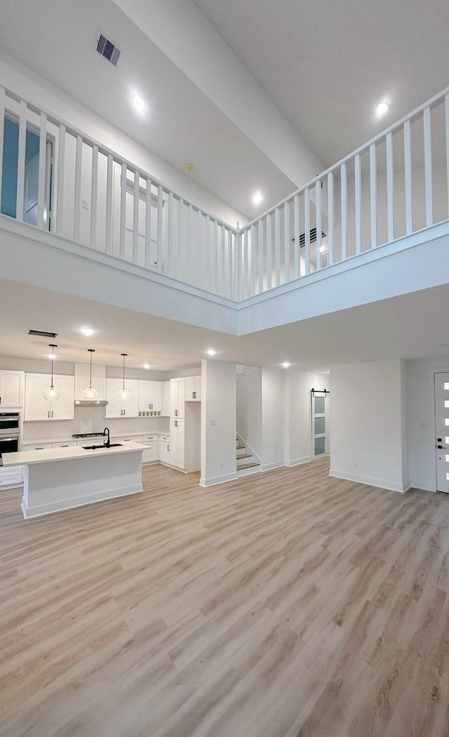 unfurnished living room featuring light hardwood / wood-style flooring, a high ceiling, and sink