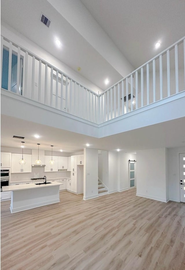 unfurnished living room featuring sink, a towering ceiling, and light wood-type flooring