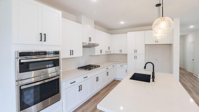 kitchen featuring sink, light hardwood / wood-style flooring, hanging light fixtures, stainless steel appliances, and white cabinets