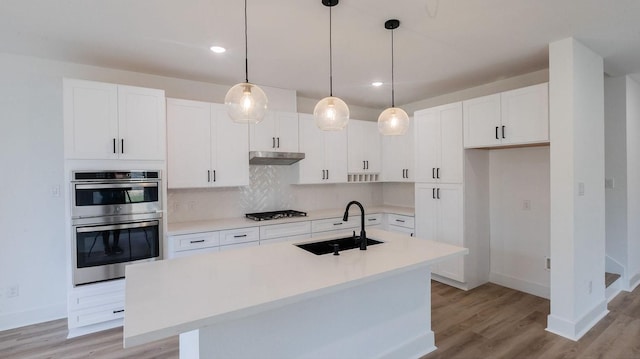 kitchen with sink, gas stovetop, hanging light fixtures, double oven, and an island with sink