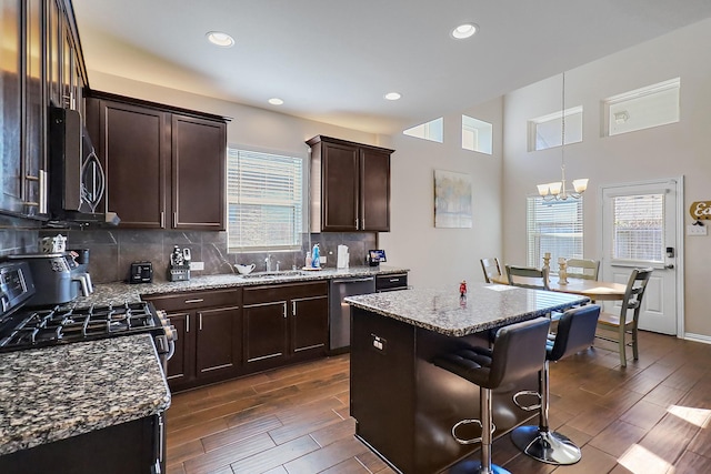 kitchen featuring appliances with stainless steel finishes, light stone countertops, a healthy amount of sunlight, a kitchen island, and decorative light fixtures