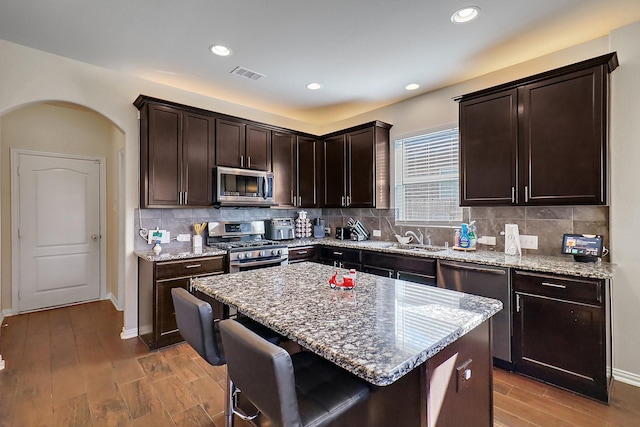 kitchen featuring light stone counters, dark brown cabinetry, appliances with stainless steel finishes, and sink