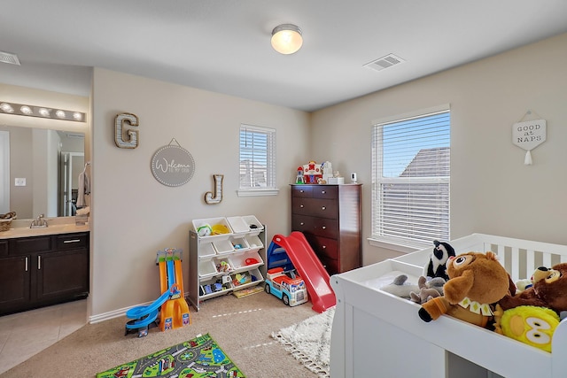 bedroom featuring a nursery area, light colored carpet, connected bathroom, and sink