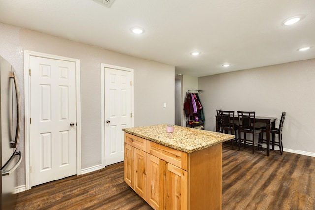 kitchen with dark hardwood / wood-style floors, stainless steel fridge, light stone counters, and a center island