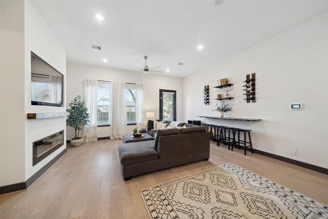 living area featuring ceiling fan, visible vents, baseboards, light wood finished floors, and a glass covered fireplace