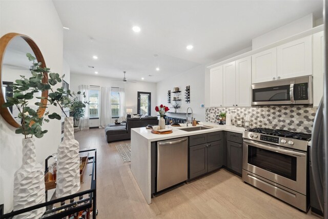 kitchen featuring white cabinets, a sink, stainless steel appliances, a peninsula, and light wood-type flooring