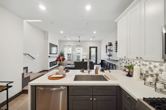 kitchen with a sink, dishwasher, light countertops, a peninsula, and white cabinetry