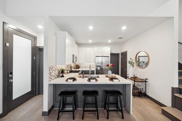 kitchen featuring a sink, stainless steel appliances, a peninsula, and light wood-style flooring
