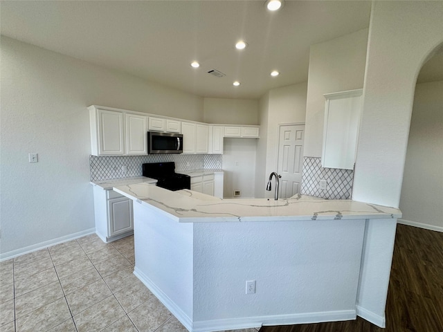 kitchen with tasteful backsplash, stove, kitchen peninsula, light stone countertops, and white cabinets