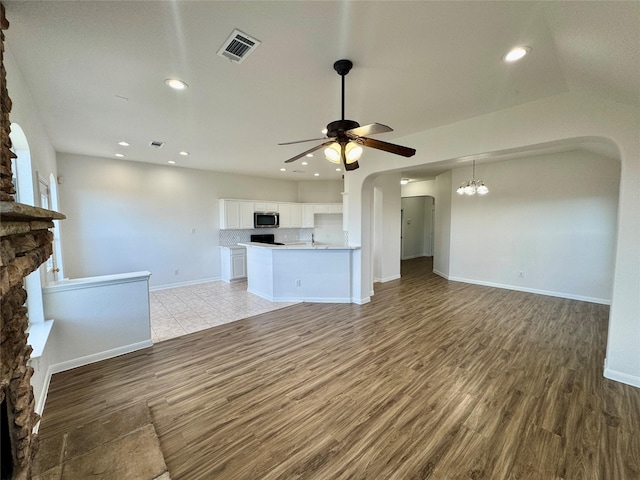 unfurnished living room with light wood-type flooring, lofted ceiling, ceiling fan with notable chandelier, and a stone fireplace