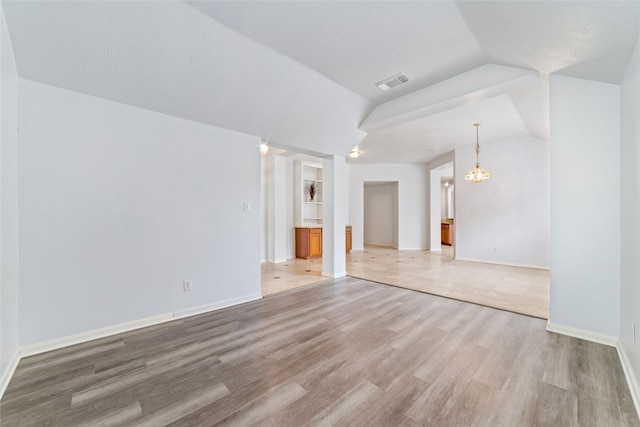 unfurnished living room featuring hardwood / wood-style floors, built in features, lofted ceiling, and a notable chandelier