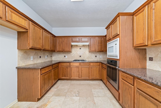 kitchen featuring white microwave, dark stone counters, backsplash, oven, and gas cooktop