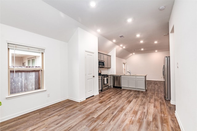 kitchen featuring appliances with stainless steel finishes, gray cabinetry, tasteful backsplash, vaulted ceiling, and light hardwood / wood-style flooring