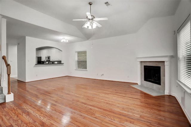 unfurnished living room featuring ceiling fan, a healthy amount of sunlight, a tiled fireplace, and light wood-type flooring