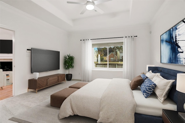 carpeted bedroom with ceiling fan, a tray ceiling, and crown molding