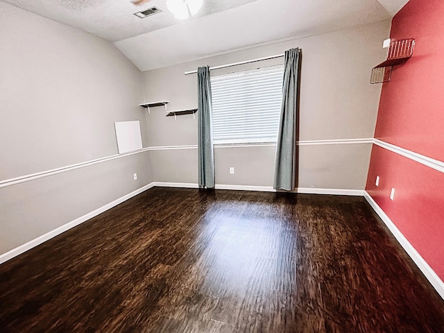 empty room featuring dark wood-type flooring, a textured ceiling, and vaulted ceiling