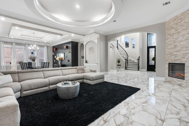 living room featuring a tray ceiling, ornamental molding, a notable chandelier, and a fireplace