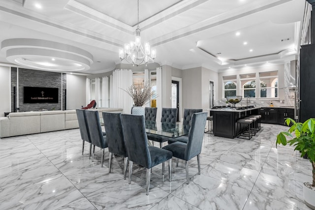 dining room with a stone fireplace, ornamental molding, a tray ceiling, and a notable chandelier