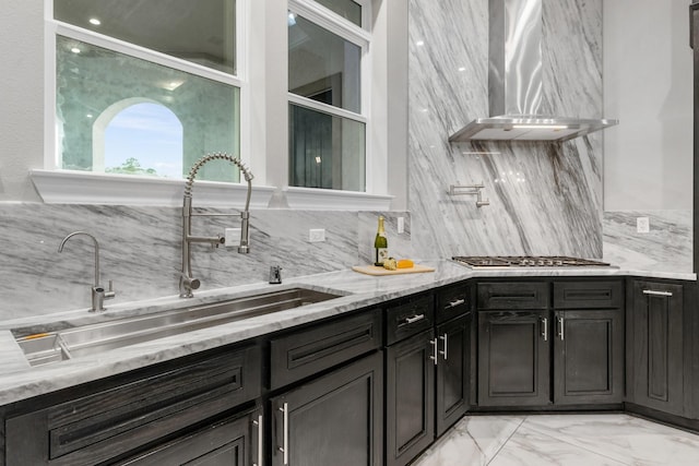 kitchen featuring tasteful backsplash, stainless steel gas cooktop, light stone countertops, wall chimney exhaust hood, and sink