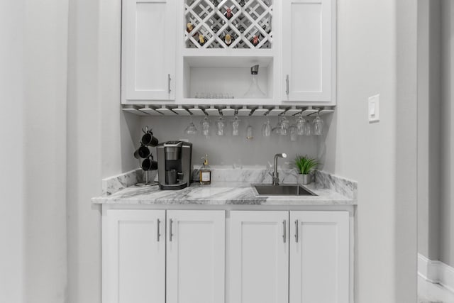 bar featuring white cabinetry, light stone counters, and sink