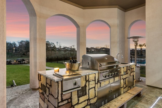 patio terrace at dusk featuring an outdoor kitchen, sink, and grilling area