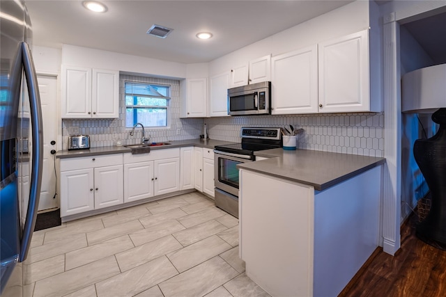 kitchen featuring decorative backsplash, dark countertops, stainless steel appliances, white cabinetry, and a sink