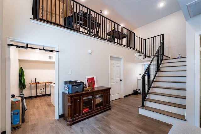 staircase with a high ceiling, wood finished floors, and visible vents