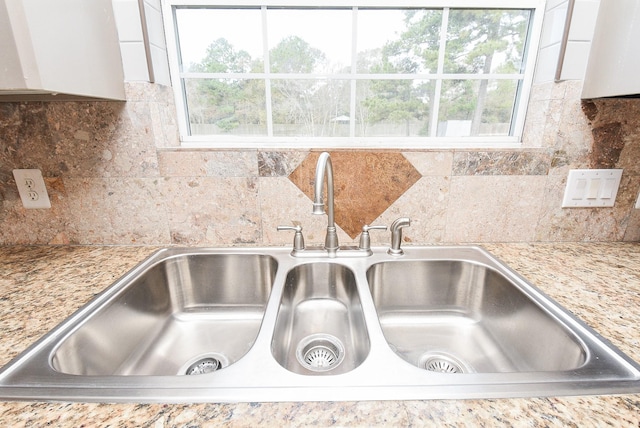 room details with white cabinetry, tasteful backsplash, light stone counters, and sink