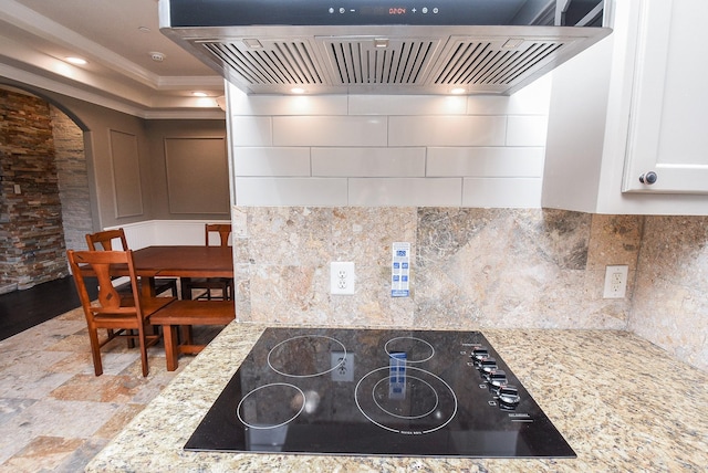 kitchen featuring backsplash, crown molding, light stone countertops, island range hood, and black electric cooktop