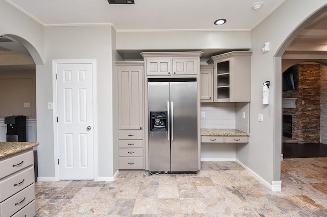 kitchen with crown molding, stainless steel fridge, tasteful backsplash, and light stone countertops