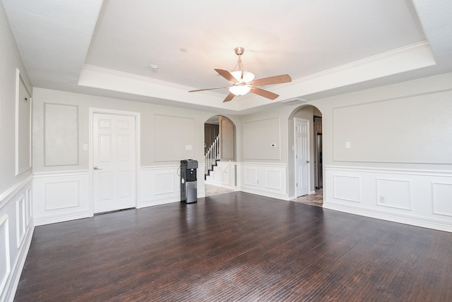 unfurnished living room with ceiling fan, ornamental molding, dark hardwood / wood-style floors, and a tray ceiling