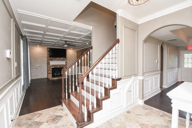 stairway with ceiling fan, a fireplace, coffered ceiling, and ornamental molding