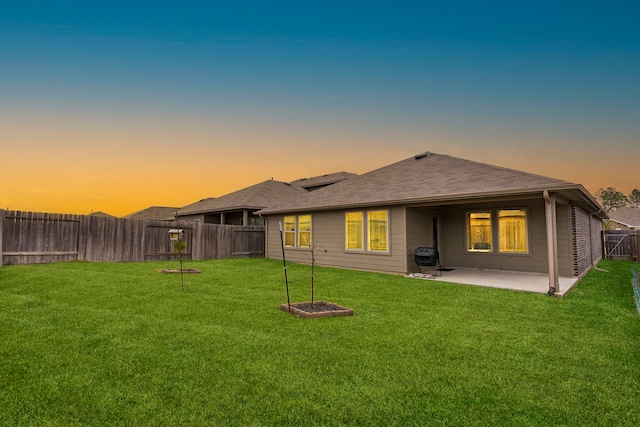 back house at dusk featuring a patio area and a yard