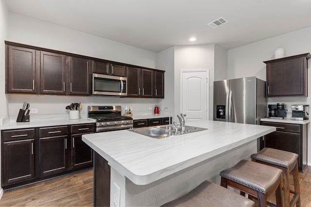 kitchen featuring a center island with sink, sink, dark wood-type flooring, appliances with stainless steel finishes, and a breakfast bar area